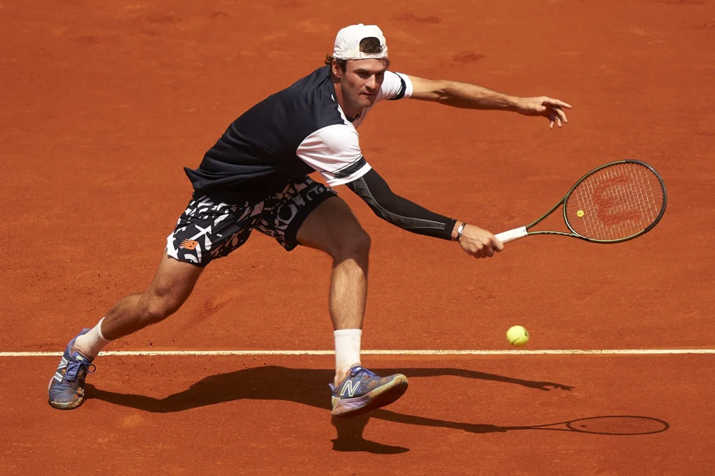 Tommy Paul smiles on clay courts, showcasing his joy and confidence ahead of a match against Carlos Alcaraz.